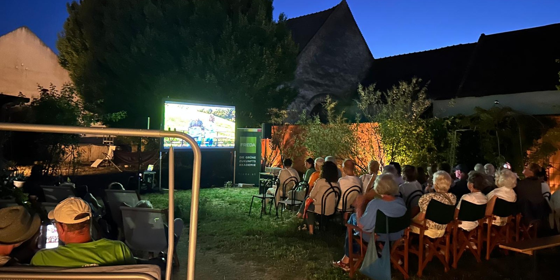 Open-Air-Kino: Publikum sitzt im Garten vor Leinwand mit Freda-Logo